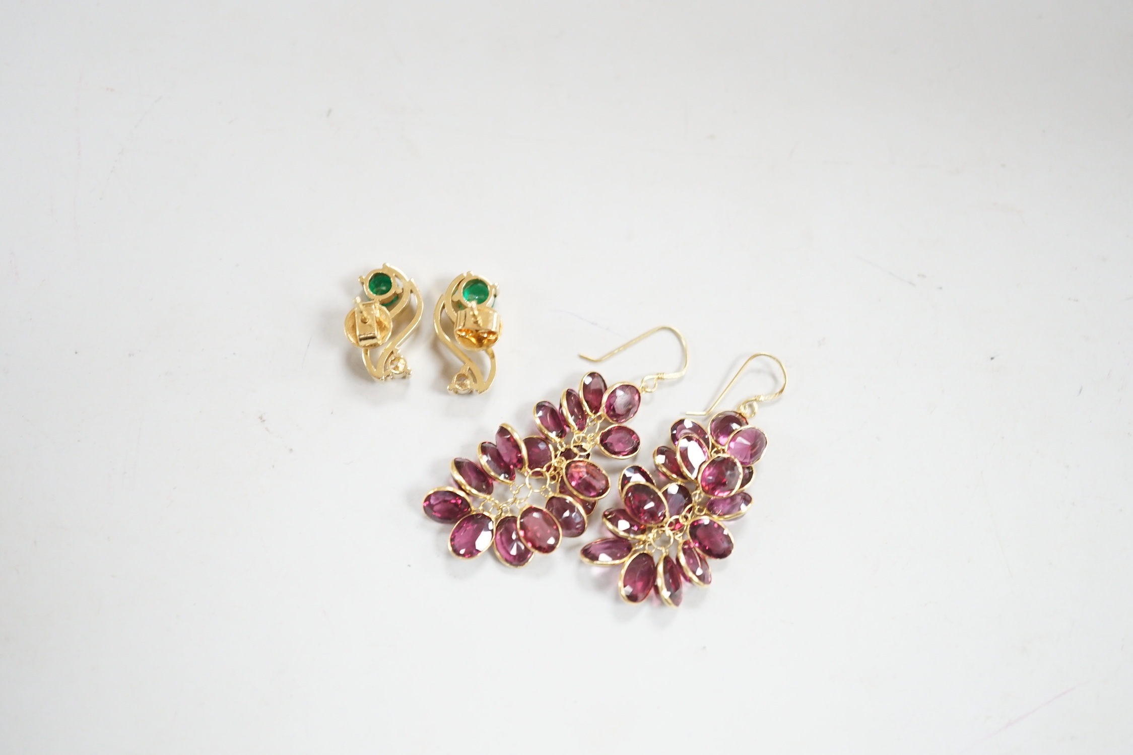 A modern pair of yellow metal, emerald and diamond set three stone ear studs, 14mm and a modern pair of yellow metal and garnet cluster set drop earrings, gross weight 8.3 grams.